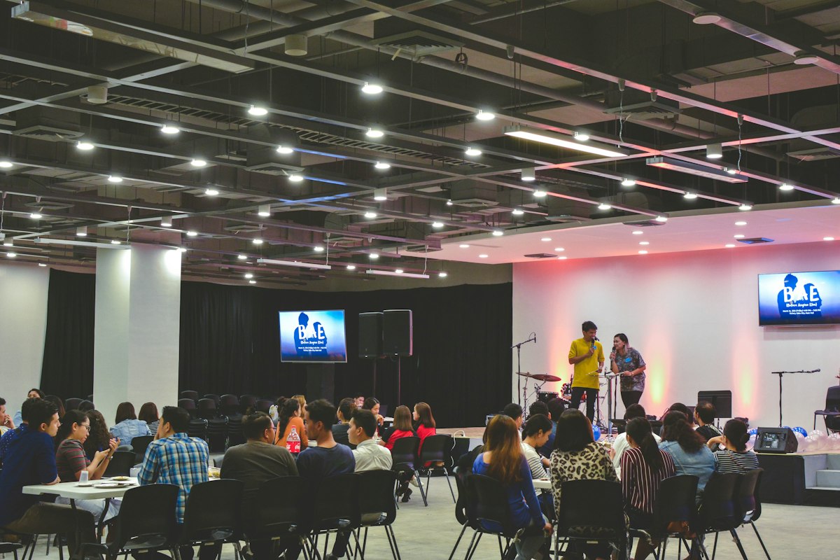 Pessoas reunidas em mesas para uma apresentação em um espaço de convivência